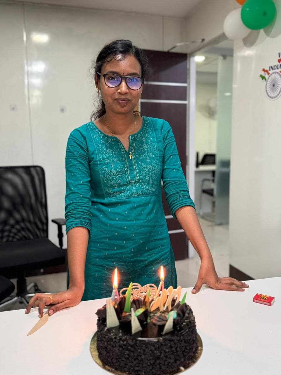 A colleague standing behind a lit birthday cake at her desk