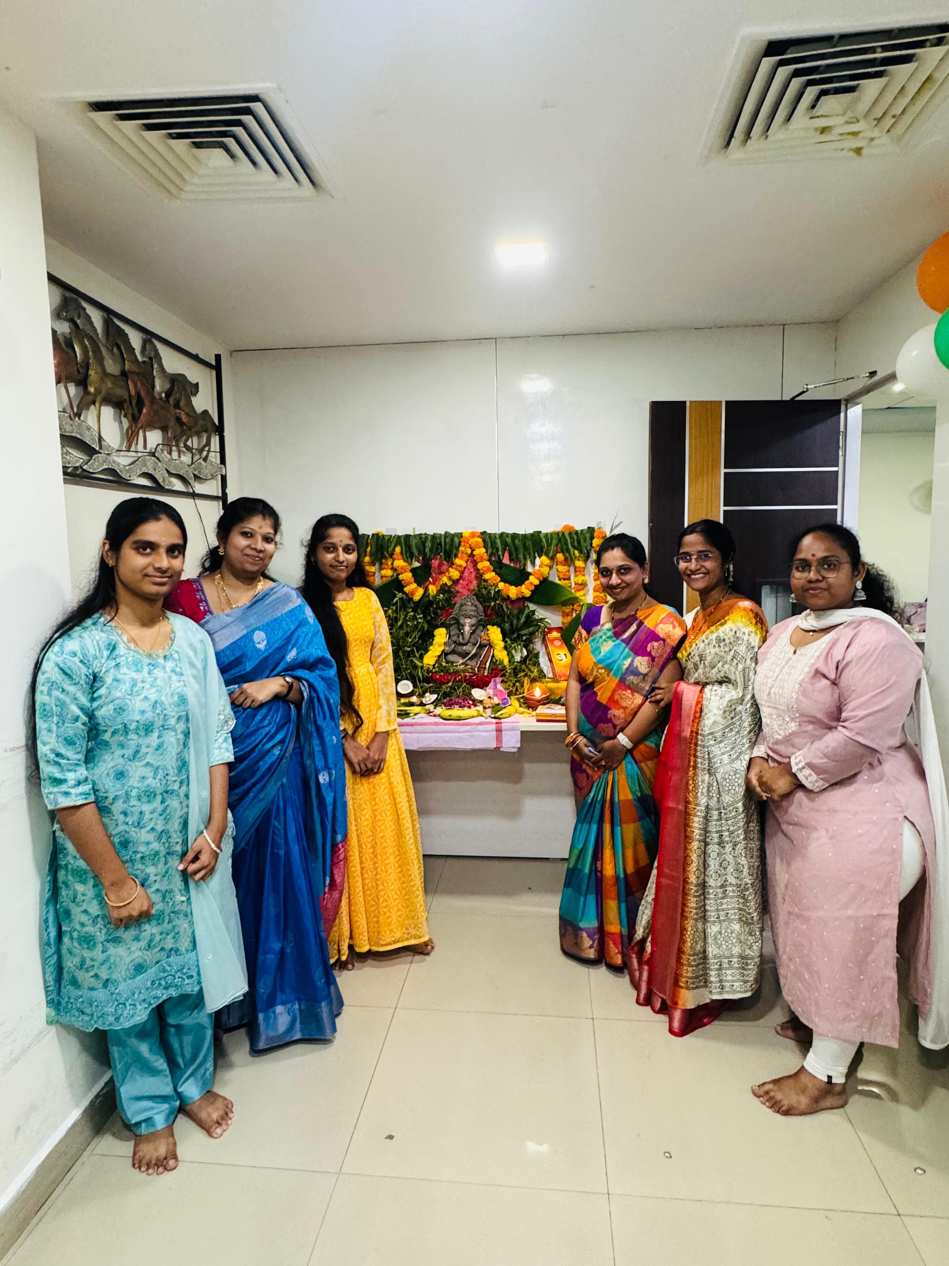 Colleagues in traditional sarees posing beside a Ganesh Chaturthi idol in the office