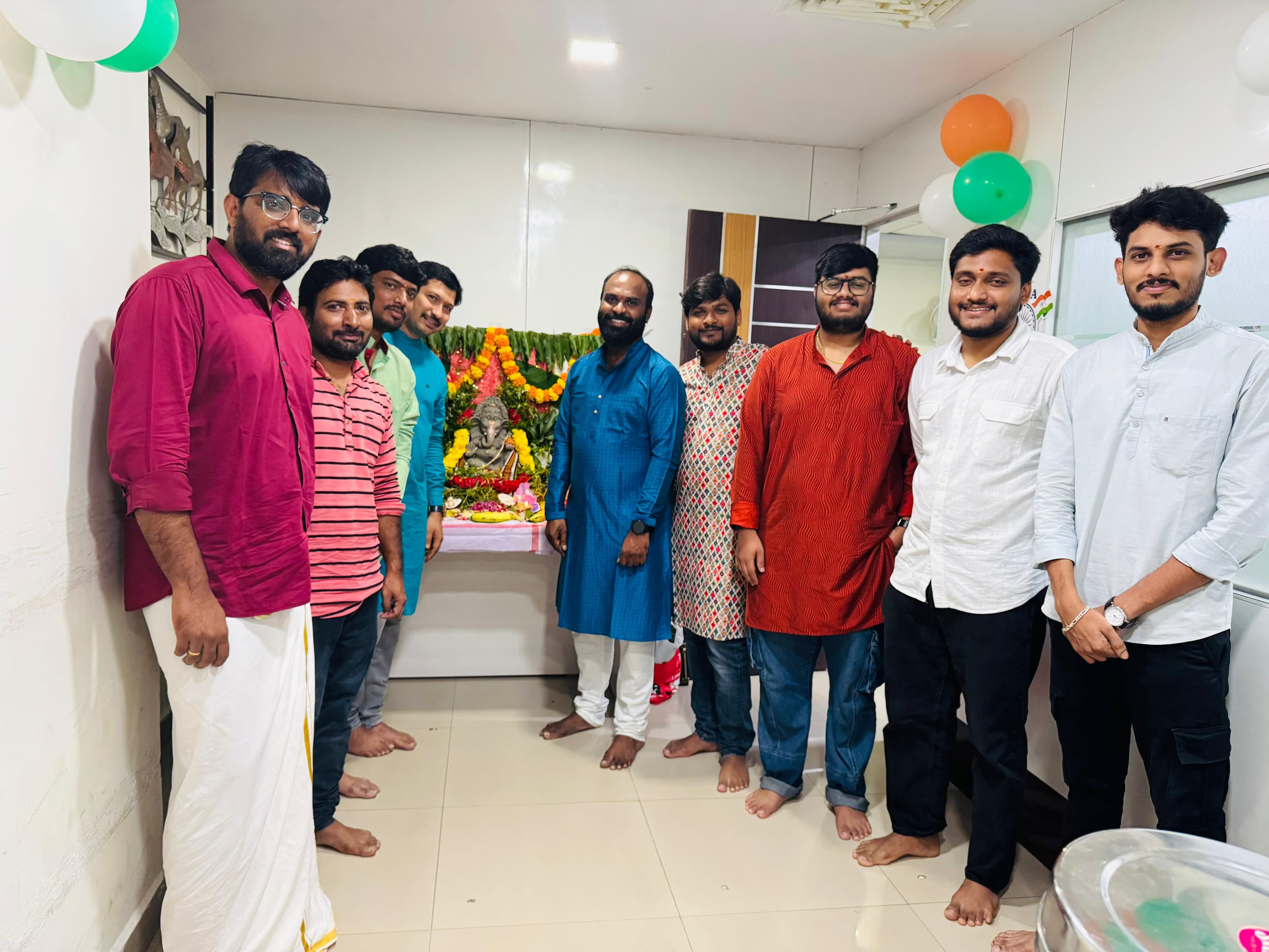 Colleagues in traditional dhotis and kurtas posing beside a Ganesh Chaturthi idol in the office