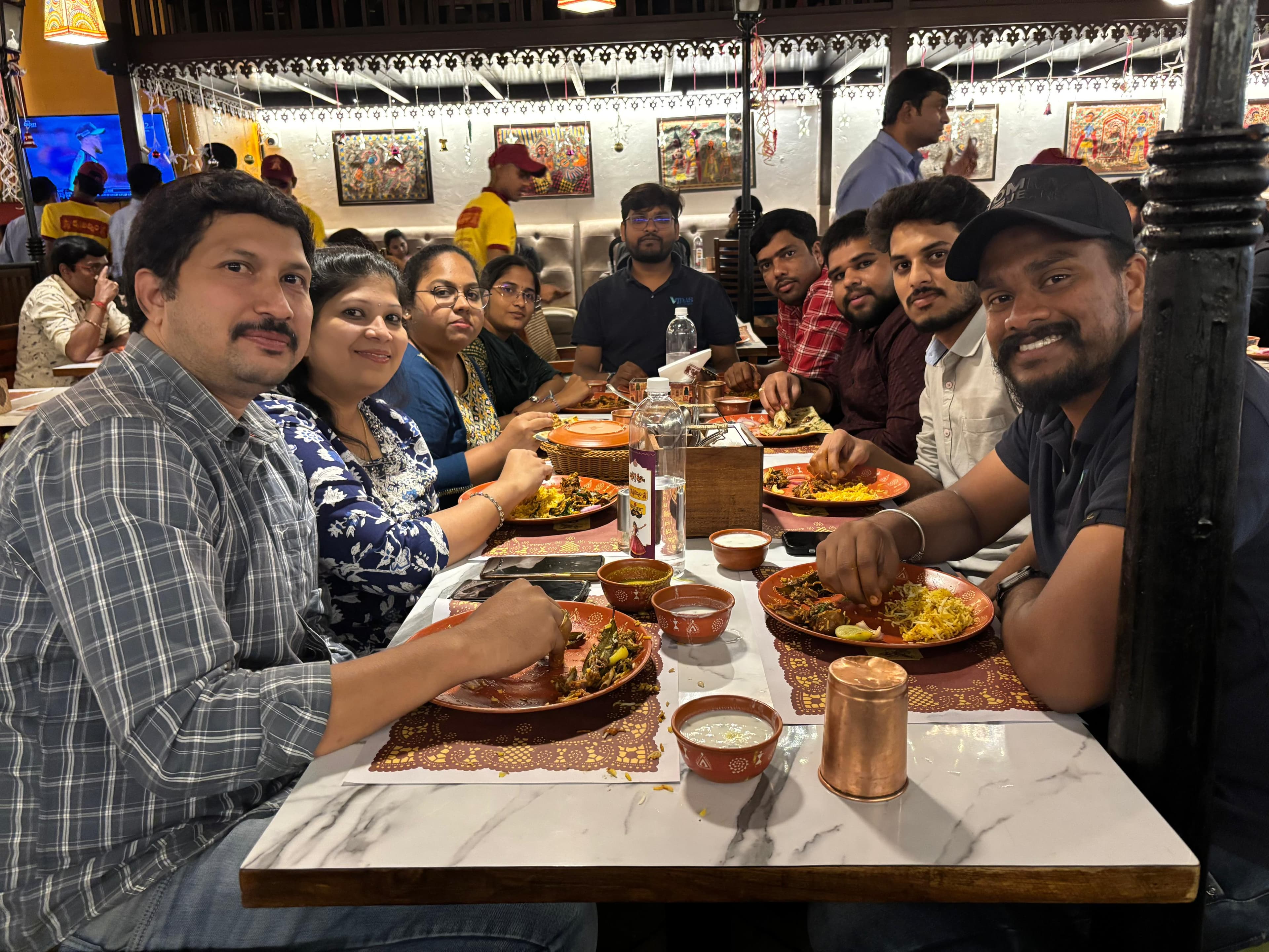 The team seated together at a long restaurant table with plates of biryani