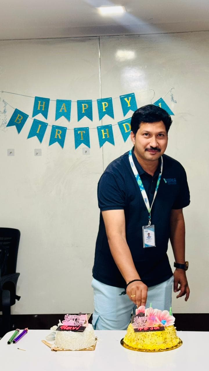 A colleague cutting a birthday cake in front of a Happy Birthday banner, with a second cake alongside