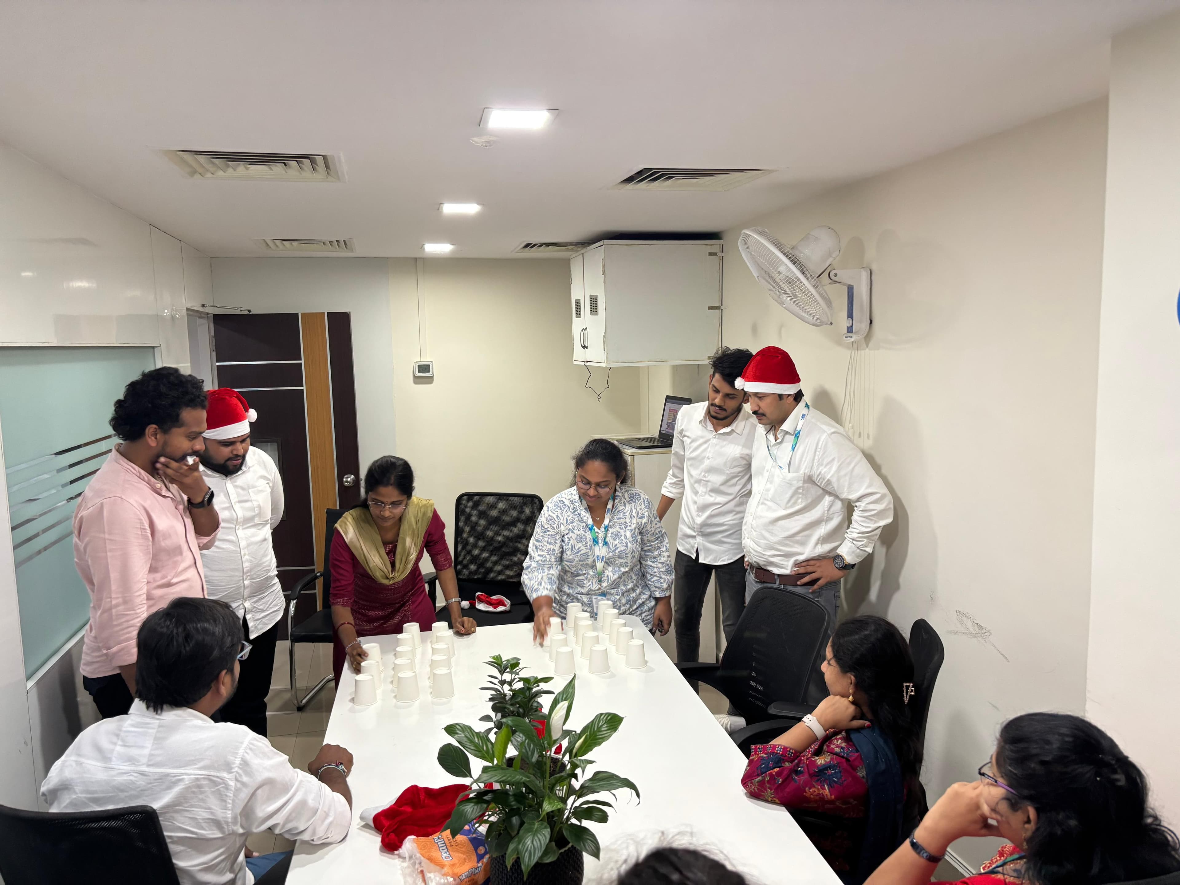 Colleagues in Santa hats gathered around a table stacking paper cups